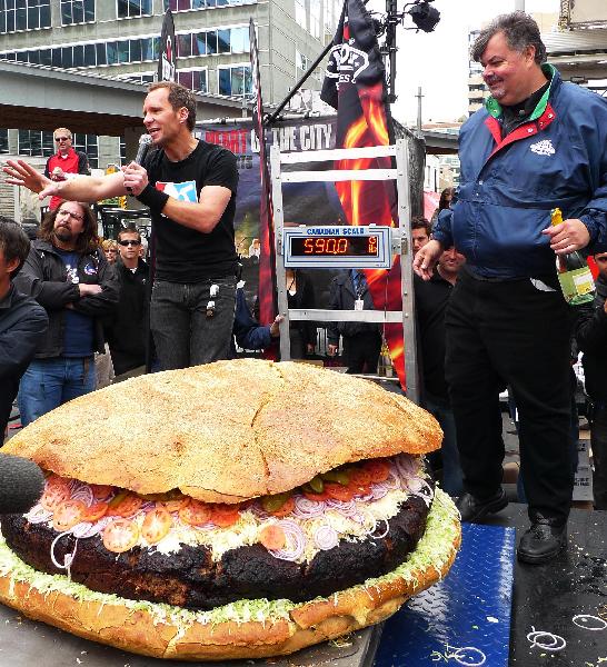 Barbecue chef Ted Reader (R) holds a bottle of champagne to celebrate the finish of a giant hamburger in Toronto, May 7, 2010. Barbecue chef Ted Reader and his assistants made a hamburger with a weight of 590 pounds (267.6 kilograms). The hamburger is waiting to be affirmed as a new Guinness World Record for world&apos;s heaviest hamburger. [Xinhua] 