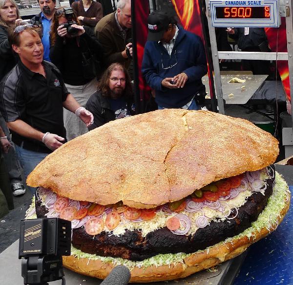 People weigh a giant hamburger in Toronto, May 7, 2010. Barbecue chef Ted Reader and his assistants made a hamburger with a weight of 590 pounds (267.6 kilograms). The hamburger is waiting to be affirmed as a new Guinness World Record for world&apos;s heaviest hamburger. [Xinhua]