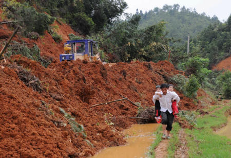 A villager carrying two children walks Sunday along a muddy road covered by a landslide in Nanding County, Jiangxi Province. The strong rainstorm, which began Wednesday, has destroyed roads in many areas of the province. [Xinhua]