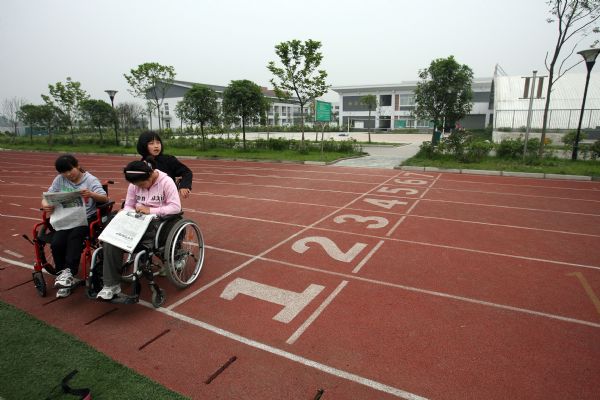 Gao Xiaoqin (L)and Zhang Chunmei from Xiaojin County read newspapers in wheelchair in You'ai School of Dujiangyan, Sichuan Province, on May 7, 2010.