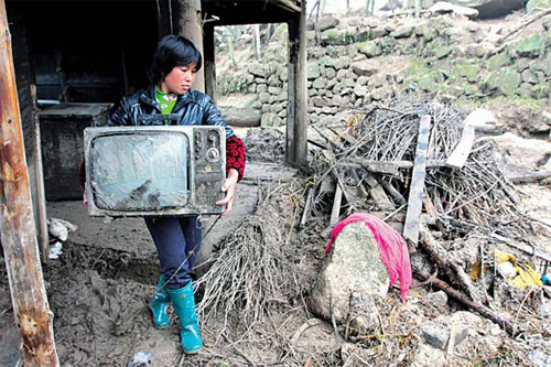 A woman carries a TV set after fl oods hit her home in Bajiaoshan village, Hunan province, on Saturday. [China Daily]