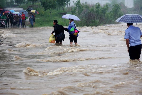 Residents walk past a flooded bridge in Wuyuan County, east China&apos;s Jiangxi Province, May 18, 2010. A heavy rainfall hit the county on May 17 and 18. More than 9,300 people have been evacuated. 