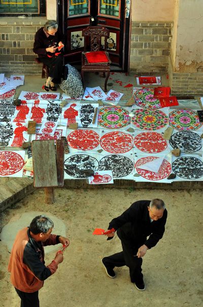 Performers dance while they show paper-cutting skills at a patio-style courtyard at a cave-house in Shanxian County in central China's Henan Province, May 19, 2010. The local government has established folk museum and tourist village for better conservation and development of the cave dwellings, an intangible cultural relics in Henan Province. [Xinhua]