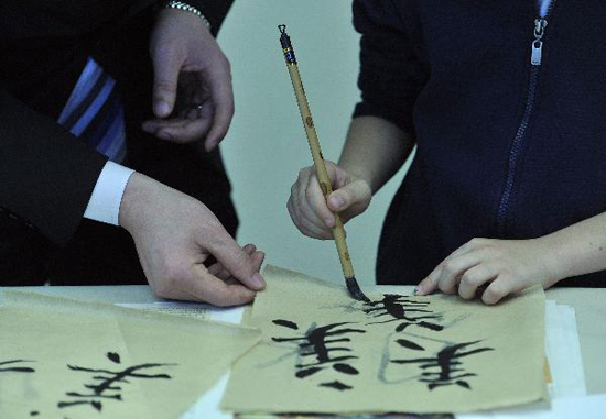 A Chinese diplomat teaches a Belgian child to use Chinese brush pen at the Open Day of the Chinese Mission to the European Union in Brussels, capital of Belgium, May 19, 2010. Some 500 local residents attended the Open Day activity to learn more about China. [Xinhua photo]