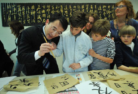 A Chinese diplomat teaches Belgian children to use Chinese brush pen at the Open Day of the Chinese Mission to the European Union in Brussels, capital of Belgium, May 19, 2010. Some 500 local residents attended the Open Day activity to learn more about China. [Xinhua photo]