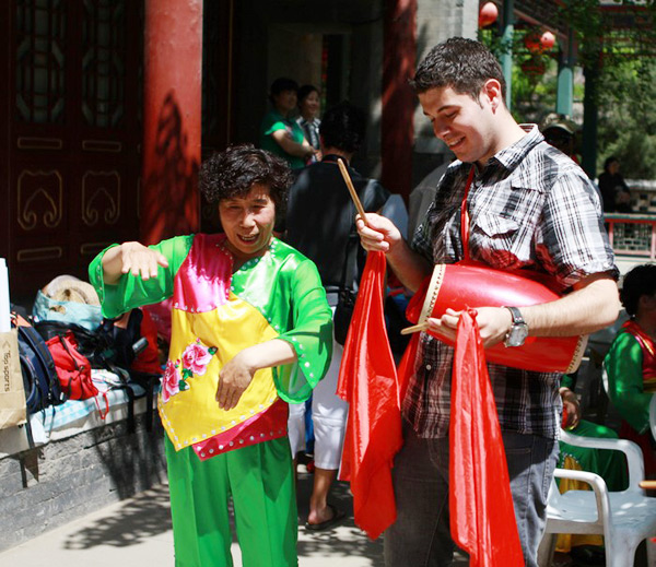 A foreign student from Beijing Language and Culture University is taught how to play a Chinese drum by a member of the drum team. A traditional Chinese drum playing competition took place on a stage erected in Beijing's Grand View Garden on Thursday, attracting hundreds of foreign students to learn the ancient art. [Photo: bicaca.com] 