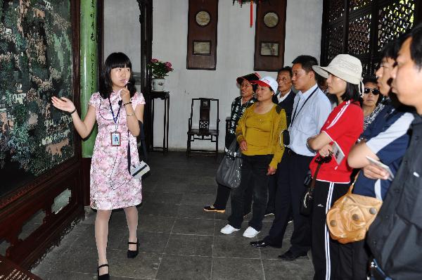 A new tour guide, wearing Chinese traditional chi-pao, explains for tourists at the Zhuozhengyuan Garden of Suzhou, east China's Jiangsu Province, May 24, 2010. A total of 13 new tour guides, who would offer free explanations for tourists, began to work at the garden Monday. [Xinhua/Zhu Guigen]