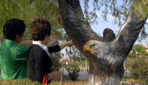 Tourists view the painting in the shape of an eagle on a tree in Yueji Garden in Beidaihe District in Qinhuangdao, north China&apos;s Hebei Province, May 24, 2010. Many animal images are painted on over 30 trees in the parks and on the streets in the city to beautify the environment. [Xinhua]