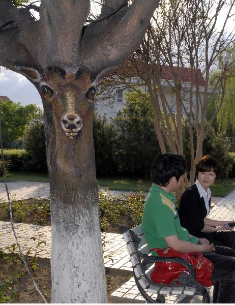 Tourists rest under a tree painted with the picture in the shape of an antelope in Yueji Garden in Beidaihe District in Qinhuangdao, north China&apos;s Hebei Province, May 24, 2010. Many animal images are painted on over 30 trees in the parks and on the streets in the city to beautify the environment. [Xinhua] 