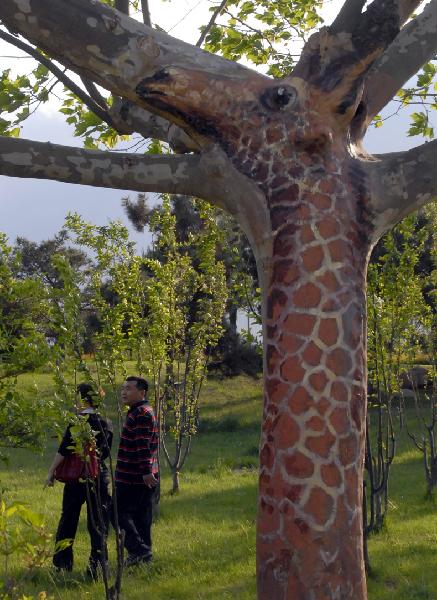 Tourists walk under a tree painted with the picture in the shape of a giraffe in the Olympic Park in Beidaihe District in Qinhuangdao, north China&apos;s Hebei Province, May 24, 2010. Many animal images are painted on over 30 trees in the parks and on the streets in the city to beautify the environment. [Xinhua]