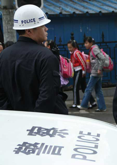A policeman supervises students as they leave their primary school Wednesday in Qingdao, Shandong Province. 