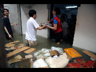 Shop assistants move goods out of the flood-hit shop. [Xinhua]