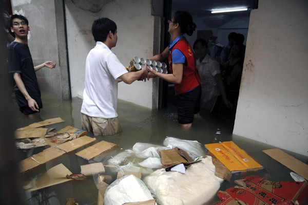 Shop assistants move goods out of the flood-hit shop.[Xinhua] 