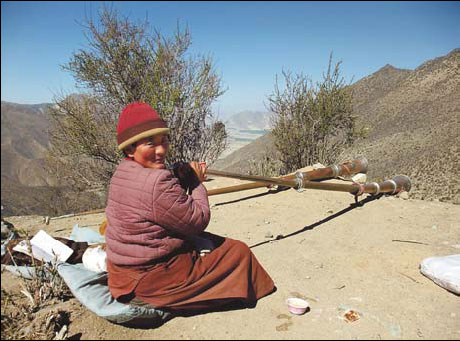 nun blows a Tibetan long horn at the entrance of Qiongse Monastery.Photos by Chen Liang / China Daily