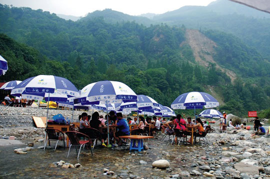 By the riverside or at foothills, clusters of people sit around a table shielded by a sun umbrella playing mah-jongg.