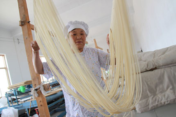 A woman makes hollow noodles on June 9, 2010, in Tangyin County of central China's Henan Province. There is a tradition of making hollow noodles by hand in the county's Yigou Town, where some craftsmen can make a dough into hollow threads as long as 200 meters by repeatedly stretching and folding it. [Shanghaidaily.com]