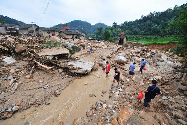 People walk past the debris after floods in Cangwu County of southwest China's Guangxi Zhuang Autonomous Region, June 16, 2010. [Xinhua]