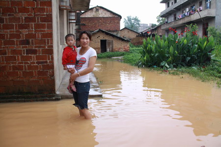  A woman, carrying her child, walks in a flooded village in Yichun, Jiangxi province, on June 17, 2010. [China Daily]