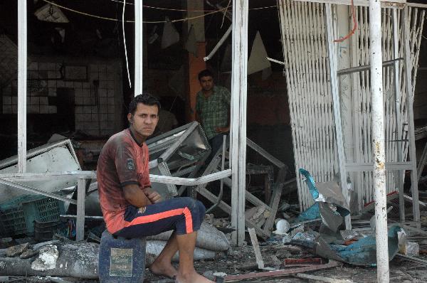 A man sits in front of a damaged store at blast site in Baghdad, capital of Iraq, June 20, 2010. At least 33 people were killed and 54 were wounded in two car bomb explosions in western Baghdad on Sunday. [Xinhua]