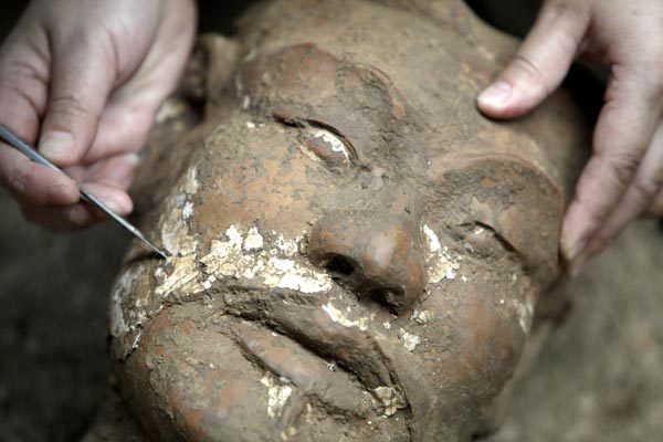 An archaeologist removes earth from the face of a newly found terracotta warrior at the excavation site inside the No 1 pit of the Museum of Qin Terracotta Warriors and Horses, on the outskirts of Xi&apos;an, Shaanxi province, June 21, 2010. [China Daily/Agencies] 