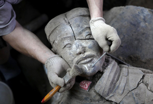 An archaeology staff member removes earth from the face of a newly found terracotta warrior at the excavation site inside the No.1 pit of the Museum of Qin Terracotta Warriors and Horses, on the outskirts of Xi&apos;an, Shaanxi province, June 21, 2010.[China Daily/Agencies] 