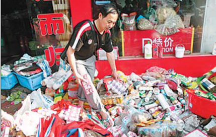 Shop owner Zhoulongping piles up boxes of milk,coke and other goods,soaked and contamintaed in the flood, for sale on Monday in Yujiang country of Jiangxi province.[China Daily]