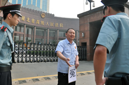 Feng Bin, wearing a judge's uniform and holding a flyer with the Chinese character yuan, meaning 'grievance' in English, quarrels with the guards of Hubei Higher People's Court at the court's front gate on Monday, June 21, 2010. [China Daily] 