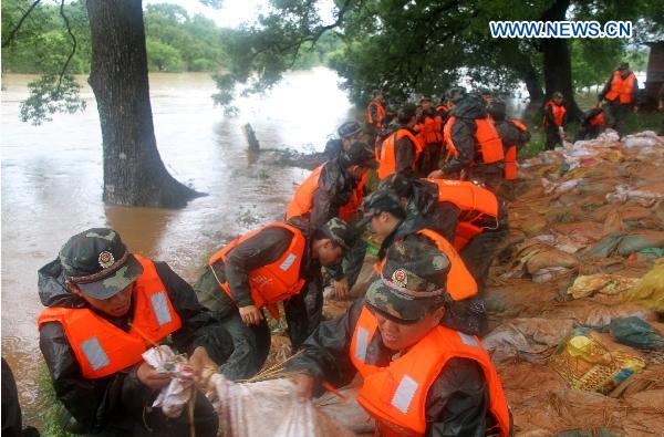 A contingent of armed policemen with the Ji&apos;an City&apos;s Detachment convey and pile up sand bags in a rush consolidation of the Fangzhou Batardeau to contain the tempestuous and surging Ganjiang River, at Liujiacun section, in Ji&apos;an City, east China&apos;s Jiangxi Province, June 24, 2010. [Xinhua]