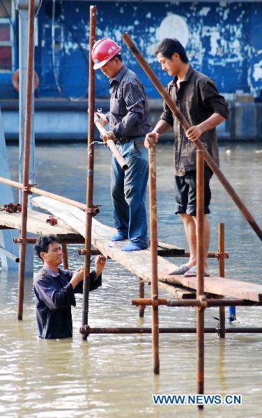 Three workers put up the frame of makeshift passage through the flooded street, at the sluice gate No. 28 on the up-surging Yangtze River at the section of Jiujiang, east China&apos;s Jiangxi Province, June 27, 2010.