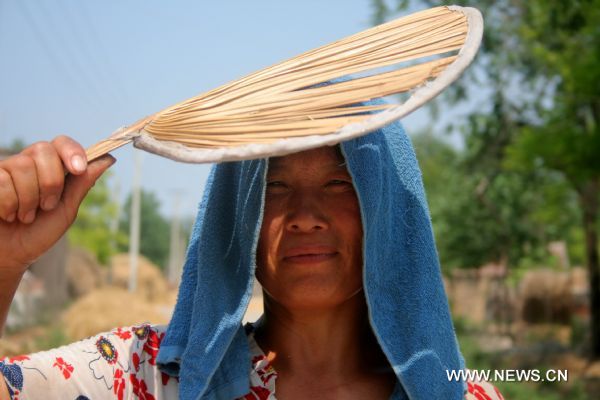 A woman wearing wet towel to cool herself off walks in Heze, east China&apos;s Shandong Province, June 28, 2010. An orange alarm of high temperature was issued by the provincial meteorological department, forecasting the highest temperature would soar to over 37 degrees Celsius in the next two days. [Xinhua]