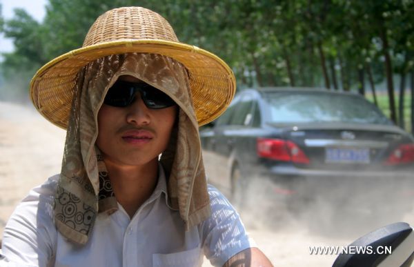 A man riding on a road wears his hat and wet towel to cool himself off in Heze, east China&apos;s Shandong Province, June 28, 2010. An orange alarm of high temperature was issued by the provincial meteorological department, forecasting the highest temperature would soar to over 37 degrees Celsius in the next two days. [Xinhua]