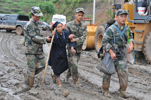 Rescue workers help an elderly woman make her way through the mud on Tuesday in Dazhai village, Guanling county of Guizhou province, where 107 villagers were buried in a landslide on Monday afternoon. [China Daily]
