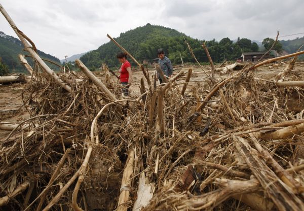 Villagers walk past farmland with piles of branches and roots at flood-hit Gaobu Village of Wangtai Township in Nanping City, southeast China's Fujian Province, June 30, 2010.