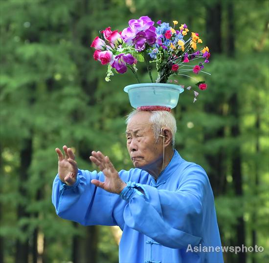 An old man practices Tai Chi (shadow boxing) while he is carrying a pot of artificial flowers on his head in Shanghai, June 30, 2010. [Photo/Asianewsphoto] 