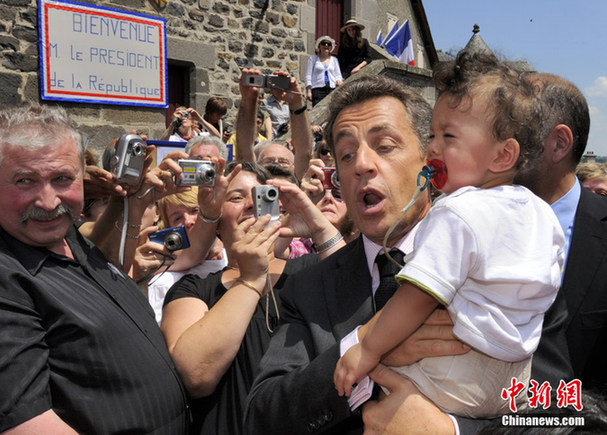 France&apos;s President Nicolas Sarkozy (C) holds a baby as he greets a crowd of onlookers during a visit at Mur-de-Barrez, Center France, July 1, 2010. [Chinanews.com]