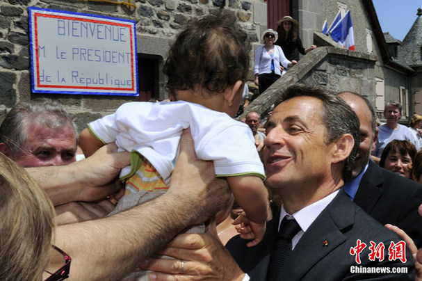 France&apos;s President Nicolas Sarkozy (C) holds a baby as he greets a crowd of onlookers during a visit at Mur-de-Barrez, Center France, July 1, 2010. [Chinanews.com]