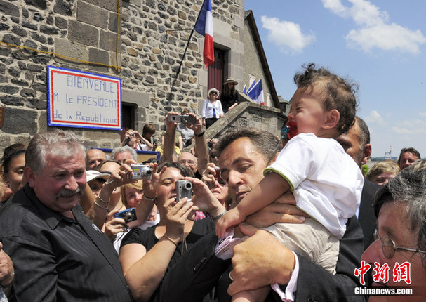 France&apos;s President Nicolas Sarkozy (C) holds a baby as he greets a crowd of onlookers during a visit at Mur-de-Barrez, Center France, July 1, 2010. [Chinanews.com]