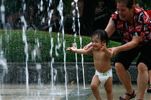 A woman helps a child to play with water at a fountain in Chongqing, July 2, 2010. [Asianewsphoto]