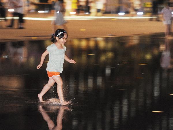 A girl walk on the ground covered by water at the World Expo Park in Shanghai, east China, on the night of July 2, 2010. More and more people prefer the night hiking in the World Expo Park to the daytime in order to avoid heat and crowded visitors. [Xinhua/Yan Yan]