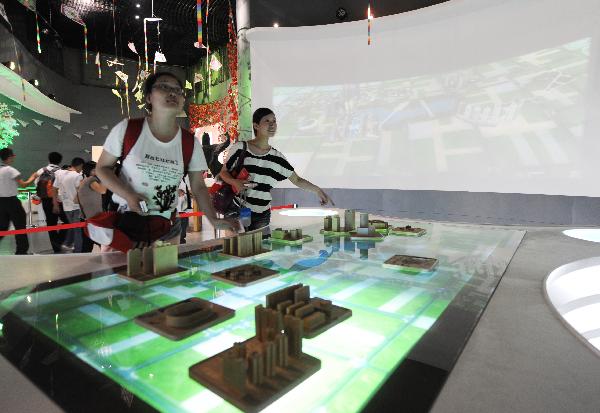 Tourists try an interactive activity at the Pavilion of Public Participation in the World Expo Park in Shanghai, east China, on the night of July 2, 2010. More and more people prefer the night hiking in the World Expo Park to the daytime in order to avoid heat and crowded visitors. [Xinhua/Yan Yan]