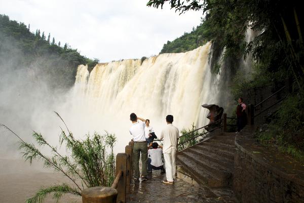 Tourists pose for pictures at the Jiulong Waterfall Scenic Zone in Luoping County, southwest China's Yunnan Province, July 2, 2010. The Jiulong Waterfall has entered a high flow season due to the enduring heavy rainfall recently. [Xinhua/Mao Hong] 