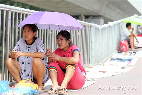 Two women sit on the street with an umbrella in hand to shield themselves from the sun in Beijing on July 4, 2010. The strongest heat wave so far this summer hit the city on Sunday, with the temperature at noon above 35 degrees Celsius. The city&apos;s meteorological center has issued this year&apos;s first yellow-coded heat alert for Sunday, warning the heat wave will continue for the next three days. [China Daily/Asianewsphoto]