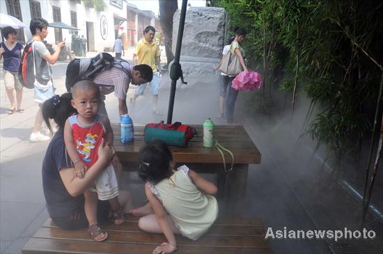 People cool down where water mist is sprayed into the air in a street in Fuzhou in East China&apos;s Fujian province, July 3, 2010. [China Daily/Asianewsphoto]