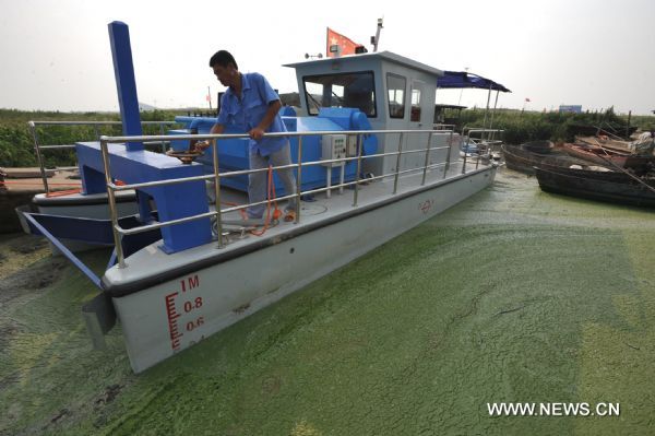 An environmental protection worker on a refloatation boat clears the blue-green algae on the Chaohu Lake in Hefei, east China&apos;s Anhui Province, July 3, 2010. Environmental protection department of Hefei and Chaohu City organized workers to clear the blue-green algae overrunning on the Chaohu Lake recently. [Xinuhua]