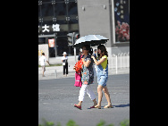 Pedestrians holding umbrella and watermelon walk across a street in Beijing, capital of China, July 5, 2010. Chinese meteorological authority said Monday hot weather continues to scorch many parts of the country. [Xinhua]