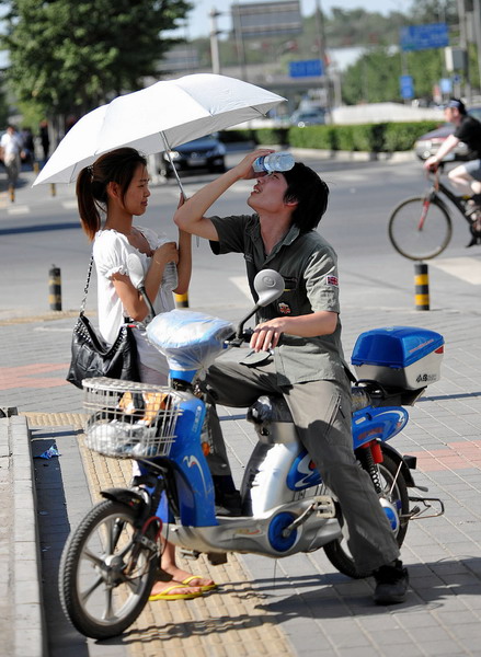 A man uses a bottle of water to cool himself off, while a woman holds up an umbrella in Beijing on July 5, 2010. [Photo/Xinhua] 