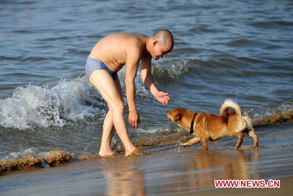 A man plays with his pet dog at seaside of the Xixiu Beach in Haikou, capital of south China's Hainan Province, July 6, 2010. The local meteorologic authority has continuously issued alarms against high temperature recently.