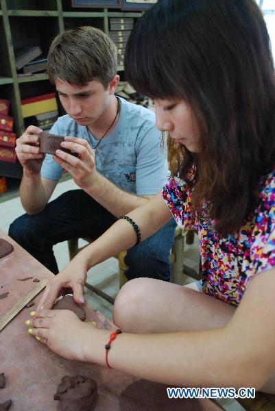 A high school student (L) from Arizona of the United States joins with a Chinese girl student in learning to make boccaro teapot at the Ceramics Town of Yixing City, east China's Jiangsu Province, July 8, 2010. Yixing city, enjoying the fame as 'ceramics capital', has been one of China's major ceramics producers for 2,000 years.