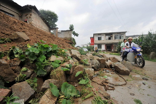 A couple drives past rubble left by rains at Yuexi county, Anhui province on July 12, 2010. Persistent rain since July 8 has affected 115,000 people in the county, inundating 450,000 hectares of farmland, damaging 365 houses and causing direct economic losses of 117 million yuan. [Photo/Xinhua]