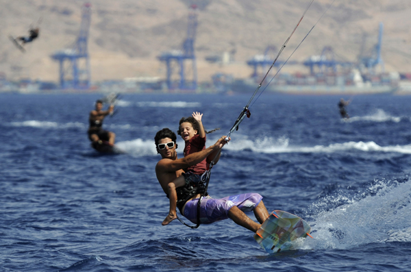 Five-year-old Michael Smila (R) waves to his mother as he kite surfs with Israeli kite surfer Eli Zarka at the Red Sea resort of Eilat July 14, 2010.[Xinhua/Reuters] 